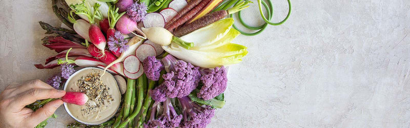 A crudite board with tahini sauce and a hand dipping a radish into the sauce.