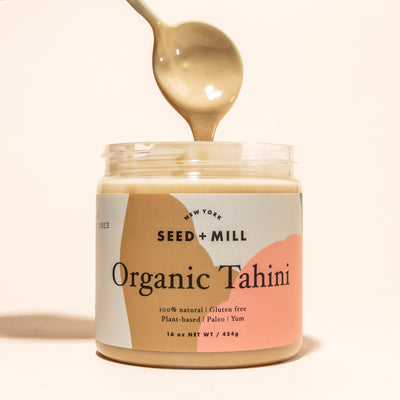 A jar of Organic Tahini with a spoon dripping tahini into it