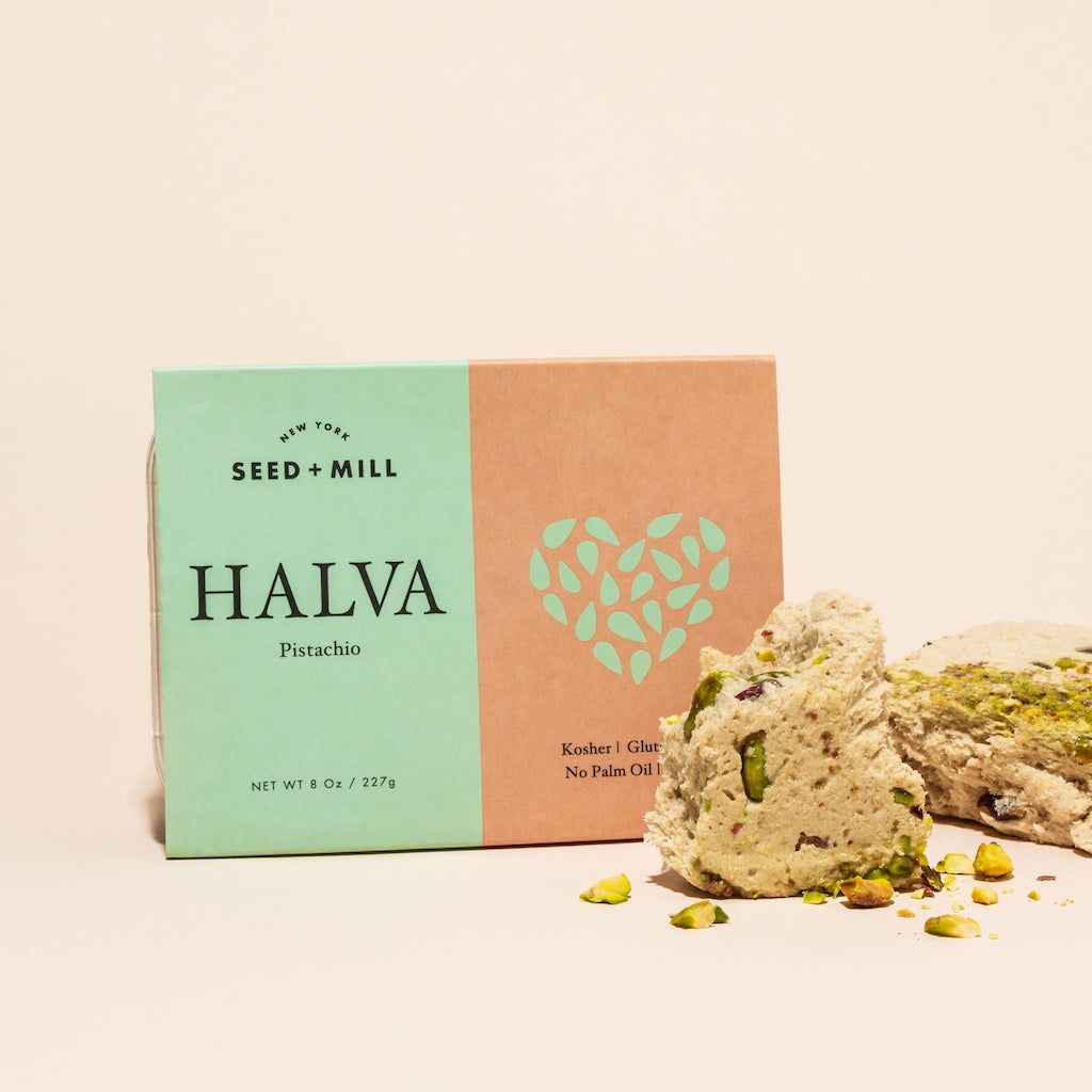 A box of pistachio halva with crumbled halva on the side.