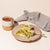 A plate with wedges of pistachio halva and a fork on top. There is a napkin on one side of the plate and a mug of cocoa on the other.