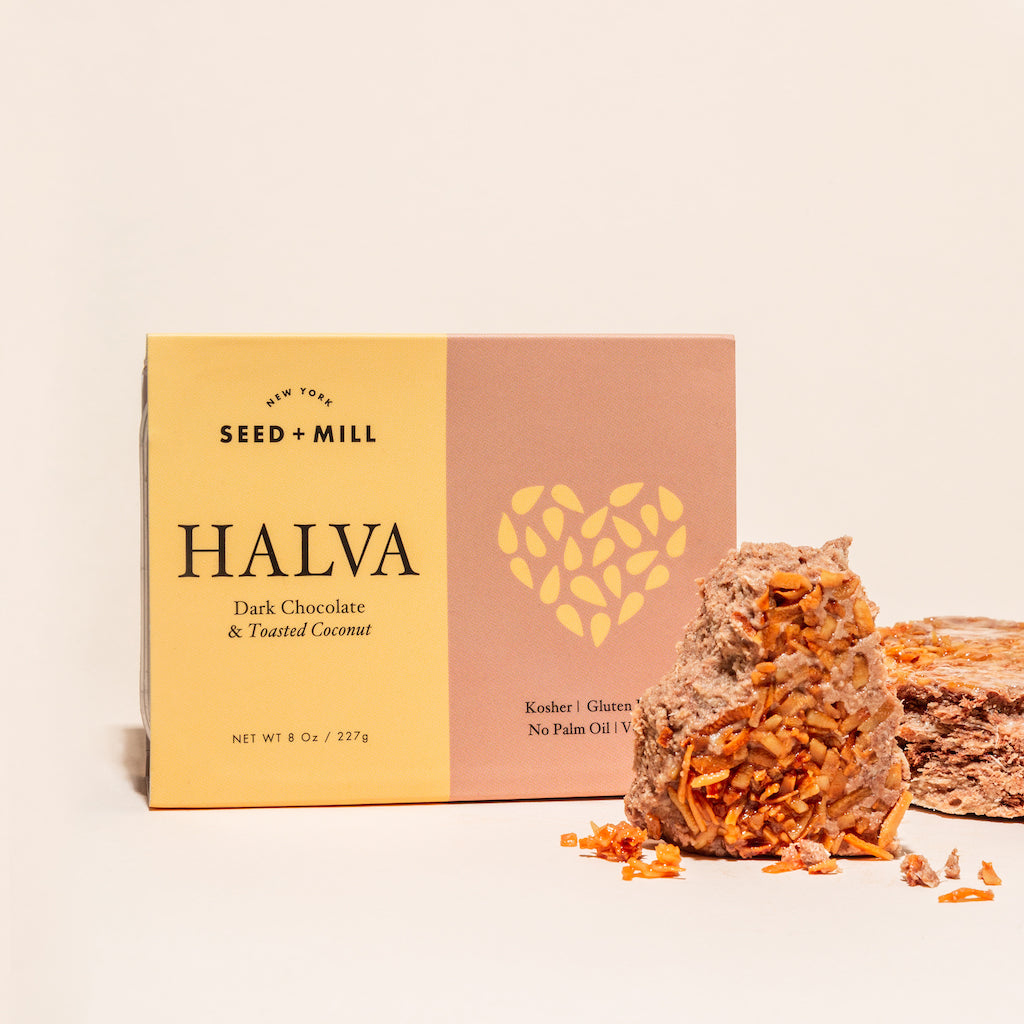 A box of dark chocolate & toasted coconut halva with crumbled halva on the side.