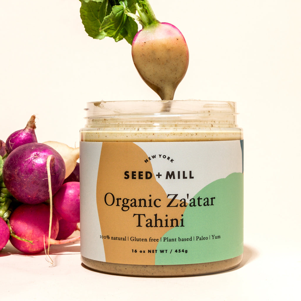 A jar of za'atar tahini next to a bunch of radishes. One radish his hanging above the tahini jar, covered in the tahini.