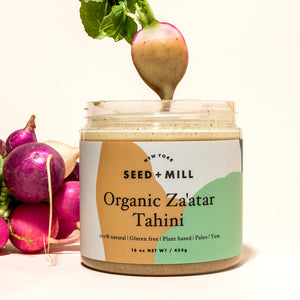 A jar of za'atar tahini next to a bunch of radishes. One radish his hanging above the tahini jar, covered in the tahini.
